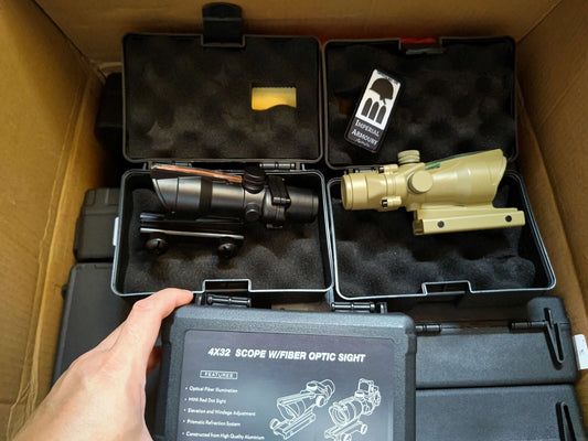 Two escape from tarkov ACOG TA01NSN scopes in a black carrying case with a hand holding the case.